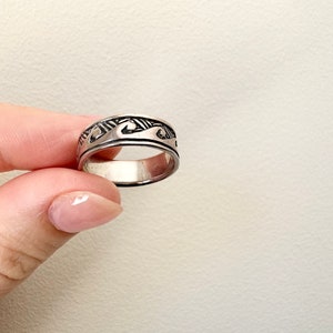 May include: A silver ring with a wave design. The ring is wide and has a textured surface.