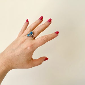May include: A silver ring with three blue turquoise stones set in a decorative design. The ring is worn on the middle finger of a hand with pink nail polish.