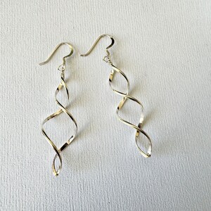 May include: A pair of silver-colored spiral drop earrings. The earrings have a hook closure and a twisted, elongated design. The earrings are displayed on a white surface.