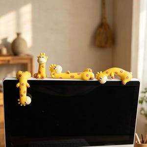 May include: A set of four yellow giraffe-shaped ornaments with brown spots, designed to sit on a computer monitor. The giraffe figurines are in different poses, adding a fun element to a desk. The figurines are made of a soft material.