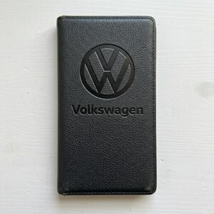 May include: Black leather wallet with the Volkswagen logo embossed on the front. The logo is a stylized 'VW' emblem inside a circle, with the word 'Volkswagen' below it.