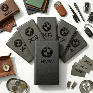Puede incluir: Un surtido de accesorios de la marca BMW, que incluyen cuadernos, una caja de madera y llaveros. Los cuadernos grises presentan el logotipo de BMW y designaciones de modelos como X1, X3, X4, X5 y X7. Otros artículos incluyen bolígrafos, una multiherramienta y una bandeja con monedas.