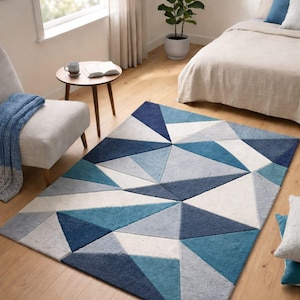 May include: A geometric patterned area rug in shades of blue, gray, and white. The rug features a repeating pattern of triangles, creating a modern design. The rug is placed on a hardwood floor in a bedroom setting.