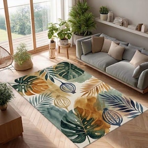 May include: A rectangular area rug with a watercolor design featuring large green monstera leaves, brown and gold palm fronds, and blue seed pod illustrations. The rug is placed on a wooden floor in a living room setting.
