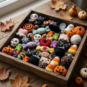 Puede incluir: Una bandeja de madera llena de un surtido de pequeñas decoraciones de fieltro con temática de Halloween, que incluyen calaveras, gatos negros, calabazas, dulces, fantasmas, arañas y caramelos coloridos, dispuestos en una colección.