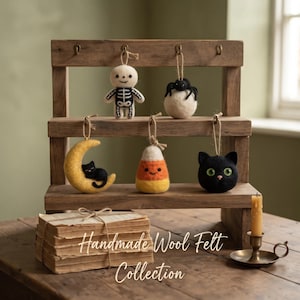 May include: A collection of five felt ornaments hanging on a three-tiered wooden stand. The ornaments include a white skeleton, a black spider on a white ball, a black cat on a yellow moon, a candy corn, and a black cat head with green eyes.