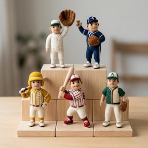 Peut inclure: Cinq figurines de joueurs de baseball en laine feutrée posées sur des blocs de bois. Les personnages portent des uniformes blancs, bleus, jaunes, rayés de rouge et verts, avec casquettes, gants et battes. Chaque figurine a une pose unique.