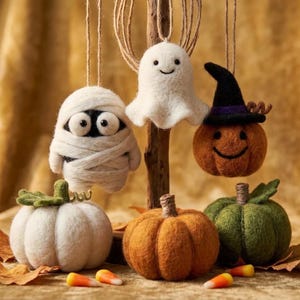 May include: A collection of felted Halloween decorations including a white mummy, a white ghost, and an orange pumpkin wearing a black hat hanging from twine. Below are three felt pumpkins in white, orange, and green with candy corn pieces.