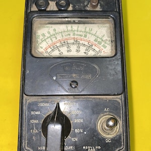 May include: A vintage black Triplett Model 666 volt-ohm-milliammeter featuring a central analog display with multiple scales, a rotary selector switch, and a toggle switch. The device includes labels for D.C., A.C., OHMS, RES-ADJ, and BLUFFTON, OHIO.