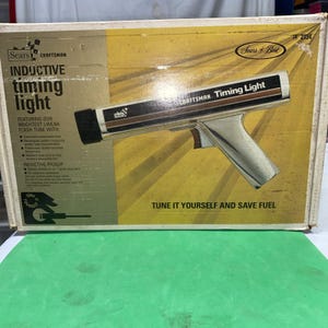 May include: A Sears Craftsman inductive timing light in its original yellow and white cardboard box. The box features the text Inductive timing light, Sears Best, and Tune it yourself and save fuel. The tool is a chrome-finished pistol-grip device.