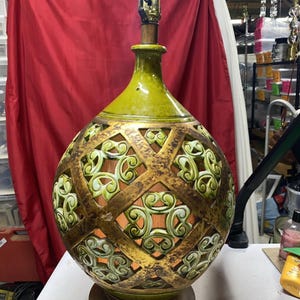 May include: A spherical ceramic table lamp featuring a lime green glaze and a brown lattice overlay with cut-out scrollwork patterns. The lamp has a narrow neck, a metal socket at the top, and sits on a circular brown base with a visible power cord.