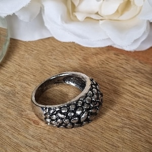 May include: A silver-toned metal ring featuring a textured, pebbled surface with a dark, oxidised finish in the recessed areas between the raised, rounded metallic bumps. The band has a wide, domed profile with a consistent, repeating pattern.