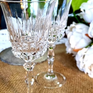 May include: Two clear crystal wine glasses featuring a vertical cut pattern on the upper bowl and a textured grid design on the lower bowl. Each glass has a slender stem and a circular base, reflecting light through the faceted glass surfaces.