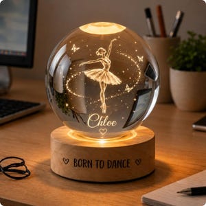 May include: A clear glass sphere night light featuring an etched ballerina and butterflies inside, illuminated by a warm glow. The name Chloe is etched on the sphere. The sphere rests on a round wooden base with the text BORN TO DANCE and hearts.