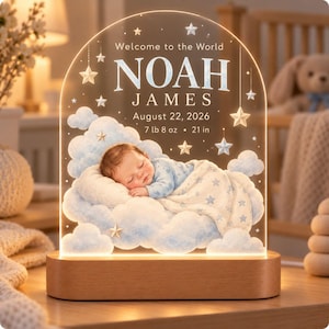 May include: An arched acrylic night light with a wooden base featuring the text Welcome to the World NOAH JAMES August 22, 2026 7 lb 8 oz 21 in. The design includes a sleeping baby on blue clouds with stars.