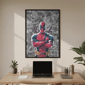May include: A framed poster featuring Deadpool in a red and black costume with crossed arms. The background is a collage of comic book panels. The poster is displayed above a wooden desk with a laptop and accessories.