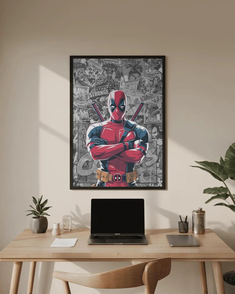 May include: A framed poster featuring Deadpool in a red and black costume with crossed arms. The background is a collage of comic book panels. The poster is displayed above a wooden desk with a laptop and accessories.