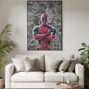 May include: A framed poster featuring the character Deadpool, in a red and black costume, with crossed arms. The background is a collage of comic book panels. The poster is displayed above a white sofa with neutral-colored pillows.