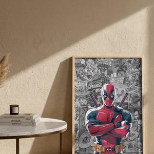 May include: A framed print featuring Deadpool in his signature red and black suit, arms crossed. The background is a collage of comic book panels. The print is displayed on a light-colored wall.