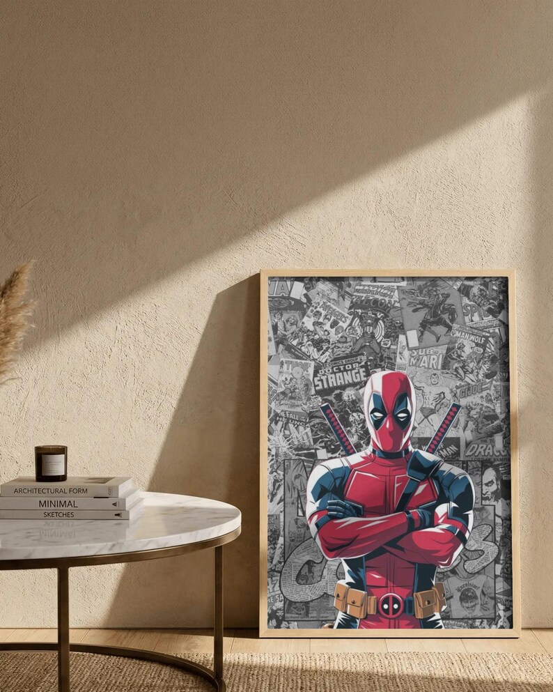 May include: A framed print featuring Deadpool in his signature red and black suit, arms crossed. The background is a collage of comic book panels. The print is displayed on a light-colored wall.