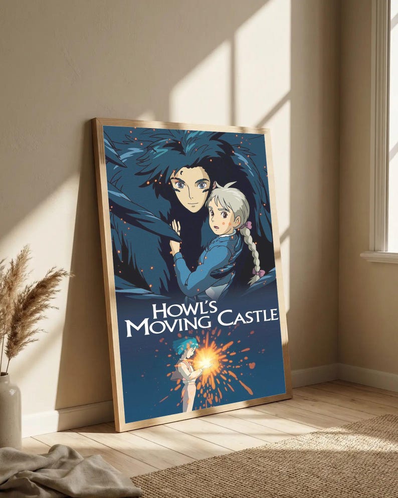 May include: A framed poster featuring artwork from the animated film "Howl's Moving Castle." The image depicts two characters in a blue and dark blue color scheme, with the film's title in white lettering. The poster is leaning against a wall.
