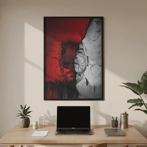 Puede incluir: Una impresión de arte mural rectangular en un marco negro que presenta un retrato de rostro dividido. El lado izquierdo muestra una figura enmascarada roja con una superficie texturizada y agrietada, mientras que el lado derecho muestra un rostro humano en escala de grises con grietas a juego.