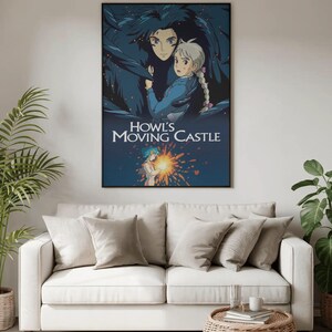 May include: A framed poster featuring artwork from the animated film "Howl's Moving Castle." The poster depicts two characters in a dark blue and light blue color scheme, with the film's title in white text. The poster is displayed above a white sofa.