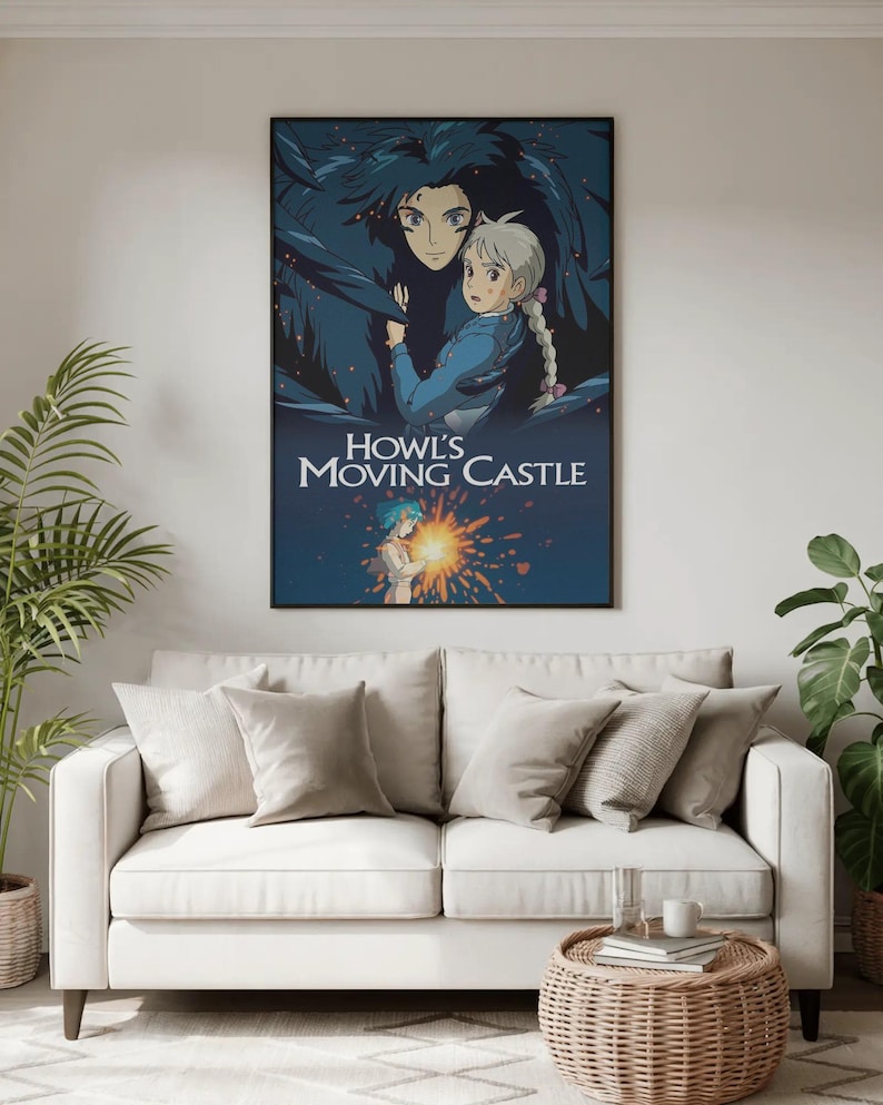 May include: A framed poster featuring artwork from the animated film "Howl's Moving Castle." The poster depicts two characters in a dark blue and light blue color scheme, with the film's title in white text. The poster is displayed above a white sofa.