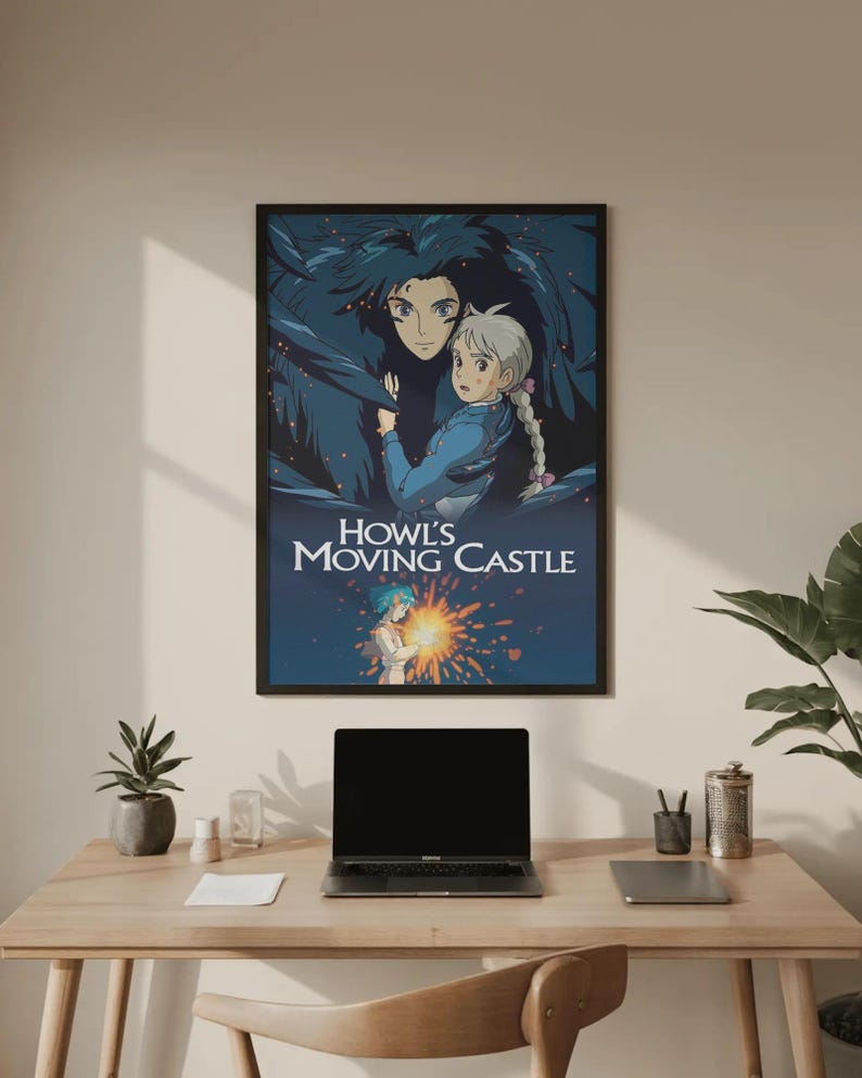 May include: A framed poster featuring artwork from the animated film "Howl's Moving Castle." The poster depicts two characters in a dark, fantastical setting, with the film's title in white text. The poster is displayed on a wooden desk.
