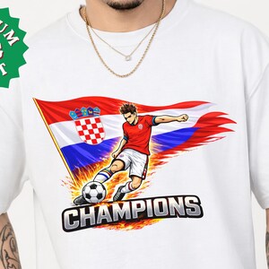 A white t-shirt with a graphic design depicting a soccer player kicking a soccer ball, with the text "CHAMPIONS" below the image.