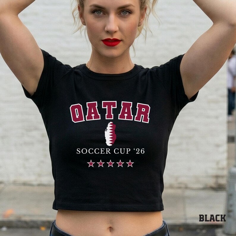 A black colored baby tee featuring a Qatar map design with "Soccer Cup '26" and five stars.