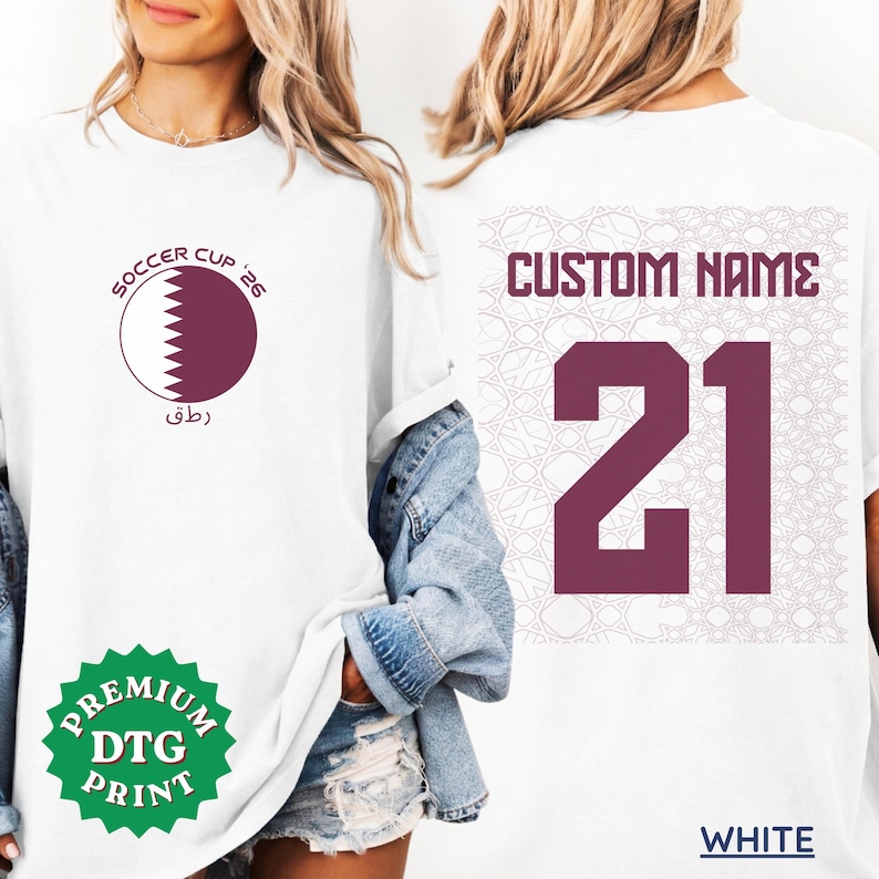 A blonde woman wearing an oversized white custom Qatar soccer t-shirt paired with denim shorts and a denim jacket hanging off her shoulder. The front shows a round Qatari flag graphic with "SOCCER CUP '26", and the back features "CUSTOM NAME 21" over a subtle geometric pattern. A green "PREMIUM DTG PRINT" badge is visible.