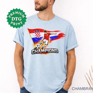 A man wearing a chambary t-shirt with a graphic of a soccer player kicking a ball and the text "CHAMPIONS" printed on it.