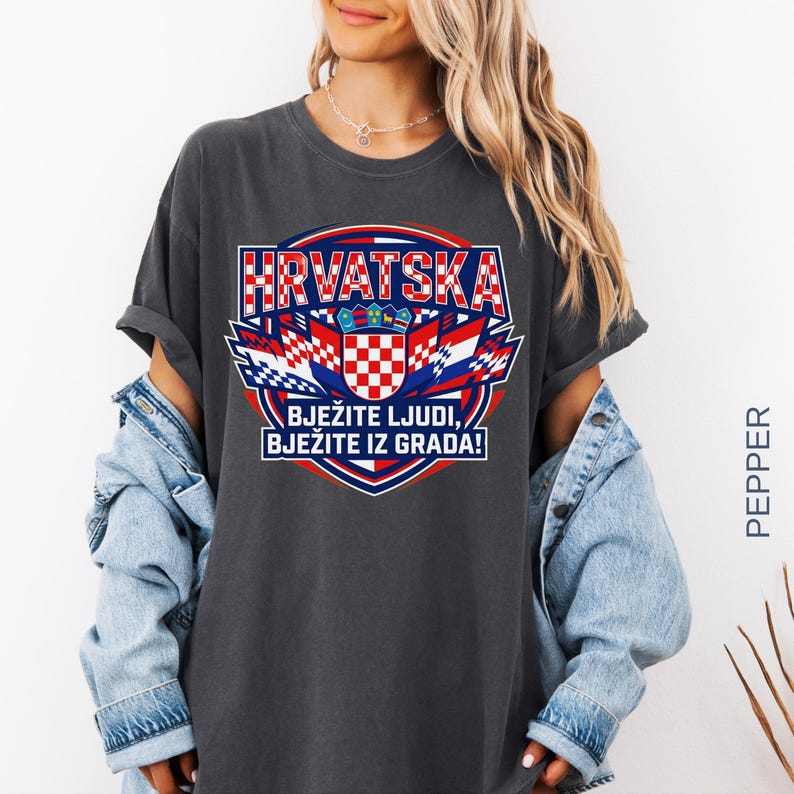 May include: Dark gray t-shirt with a Croatian flag design. The design includes the word "HRVATSKA" in red and white, along with the text "BJEŽITE LJUDI, BJEŽITE IZ GRADA!" in blue and white. The shirt has rolled-up sleeves.