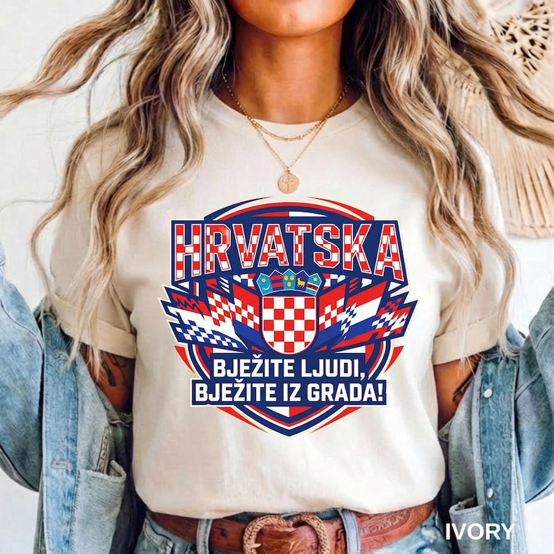 May include: Ivory-colored t-shirt featuring a Croatian flag design. The graphic includes the word "HRVATSKA" in red and white, along with the text "BJEŽITE LJUDI, BJEŽITE IZ GRADA!" in blue and white. The shirt has short sleeves.