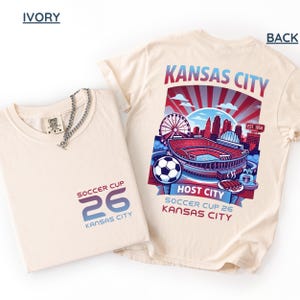An ıvory back print shirt the front features a minimal "SOCCER CUP 26 KANSAS CITY" logo.