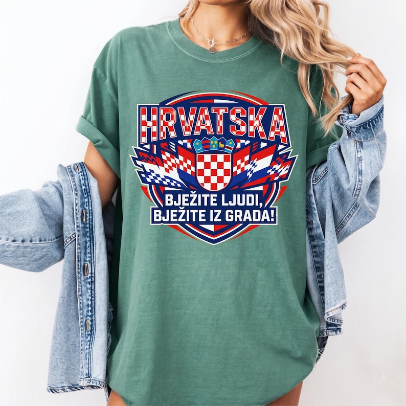 May include: A green t-shirt featuring a Croatian flag design with the word "HRVATSKA" in red and white block letters. The design includes a checkered shield and the text "BJEŽITE LJUDI, BJEŽITE IZ GRADA!"