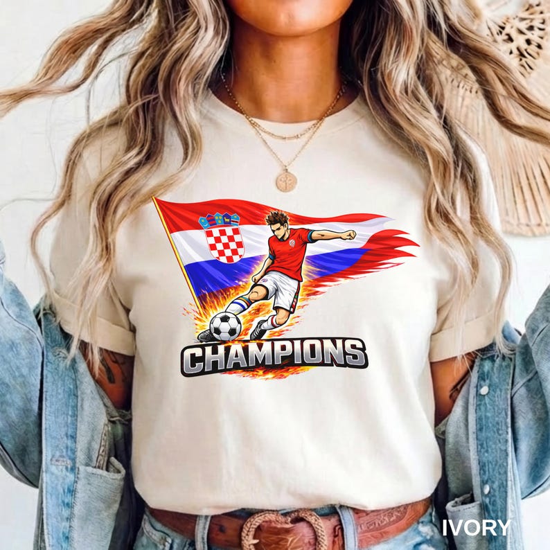A person wearing a ivory t-shirt with a graphic of a soccer player kicking a ball, along with the text "CHAMPIONS" printed on it.