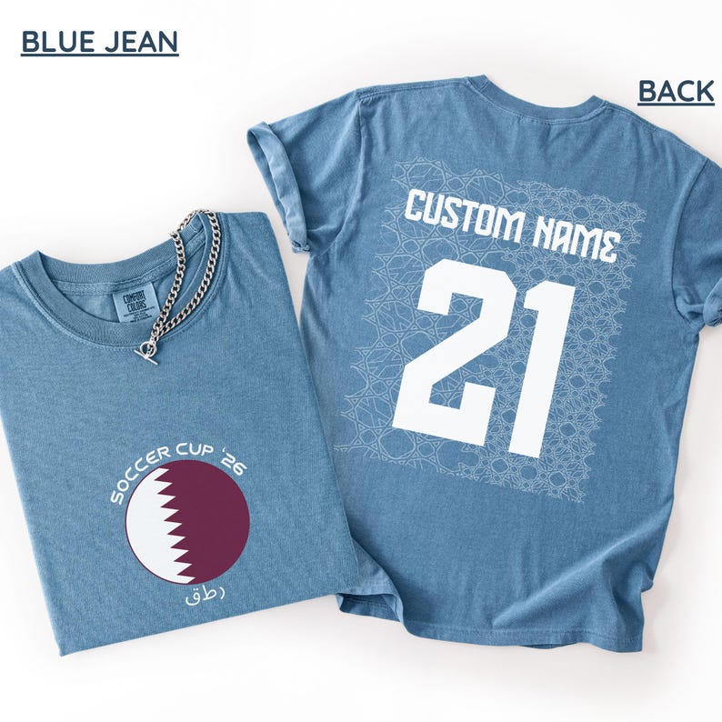 Flat lay of a Blue Jean shirt. The front folded view displays the circular maroon and white serrated Qatar flag graphic with curved "SOCCER CUP '26" typography. The flat back view shows a large white square geometric Arabic mosaic pattern under a bold white "CUSTOM NAME" and number 21.