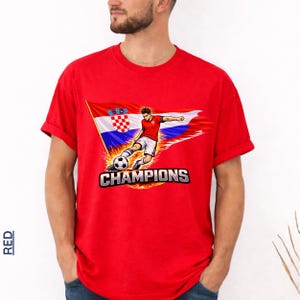A man wearing a red t-shirt with a graphic of a soccer player kicking a ball and the text "CHAMPIONS" printed on it.
