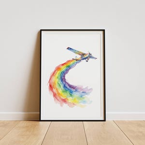 May include: A framed watercolor print depicts a small airplane trailing a vibrant rainbow. The artwork features a blue, yellow, and orange plane against a white background. The rainbow arcs gracefully, showcasing a spectrum of colors.