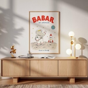 Vintage Babar astronaut printable wall art featuring the beloved French storybook elephant dressed in a detailed white astronaut spacesuit with his iconic golden crown, standing on the moon while waving toward planet Earth. The whimsical illustration includes a classic red and white rocket ship, sparkling stars, a lunar landscape with craters, and a colorful view of Earth floating in outer space.