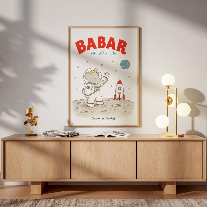 Vintage Babar astronaut printable wall art featuring the beloved French storybook elephant dressed in a detailed white astronaut spacesuit with his iconic golden crown, standing on the moon while waving toward planet Earth. The whimsical illustration includes a classic red and white rocket ship, sparkling stars, a lunar landscape with craters, and a colorful view of Earth floating in outer space.