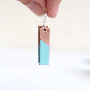 May include: A pair of dangle earrings with a rectangular copper and turquoise design. The earrings are silver and have a simple hook closure.