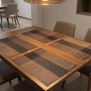 Op de afbeelding: Een houten eettafelset met vier rechthoekige placemats. Elke placemat heeft een gestreept patroon in bruin- en zwarttinten. De tafel is omringd door stoelen met lichtbruine bekleding.