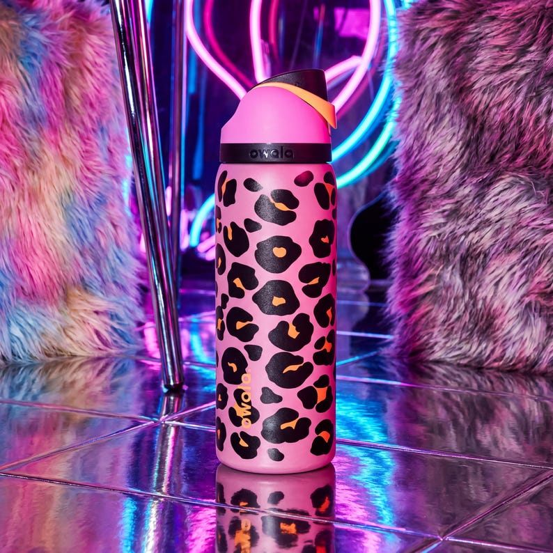 May include: Pink water bottle featuring a black and orange leopard print pattern. The bottle has a pink lid with a black and orange accent. The brand name "owala" is printed on the bottle.