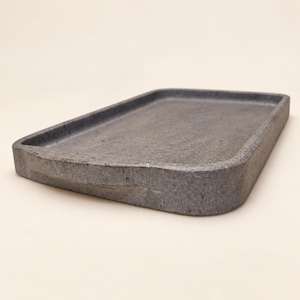 May include: A rectangular tray with a dark grey, speckled, stone-like texture. The tray features a flat, recessed centre surface surrounded by thick, raised edges with rounded corners, presenting a solid and uniform appearance throughout.