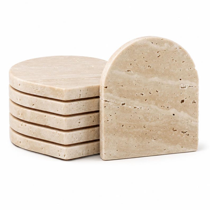 May include: A stack of six beige stone coasters with rounded corners and a matching arched piece. The coasters are made of a natural stone material with visible veining and small holes, suggesting a travertine or similar stone.
