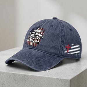 May include: A navy blue baseball cap with a curved brim. The cap features a distressed American flag design with a cross and the text "NORMAL ISN'T COMING BACK JESUS IS." A smaller flag with a red cross is on the side.