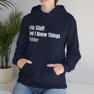May include: Navy blue hooded sweatshirt with the text "I Fix Stuff And I Know Things Welder" in white. The sweatshirt has a front pocket and a drawstring hood. The garment is made of a soft material.